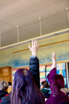 children raising hands in classroom 