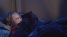 a little boy reading a Bible in bed 
