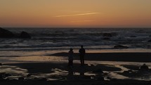 Couple watches ocean waves hit coastline rocks right after sun sets 