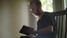 young man sitting in a chair reading a Bible 