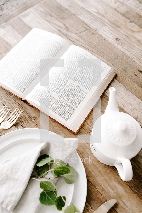 opened Bible on a table with tea pot and plate and napkin