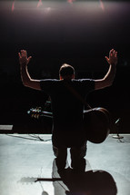 Worship leader worshipping, kneeling on stage with his guitar 