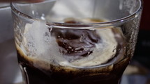 Slow motion - hand of a person putting ice cubes into a glass of coffee
