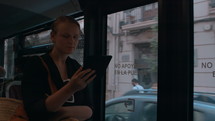A young woman holds an e-reader in her hand and reads something while riding in a city bus, standing at the door
