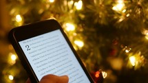 reading a Bible verse off a phone in front of a Christmas tree 