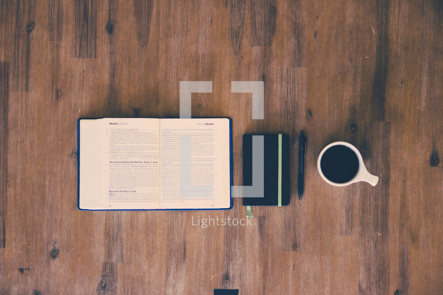 open Bible, journal, pen, and coffee mug on a wood floor 