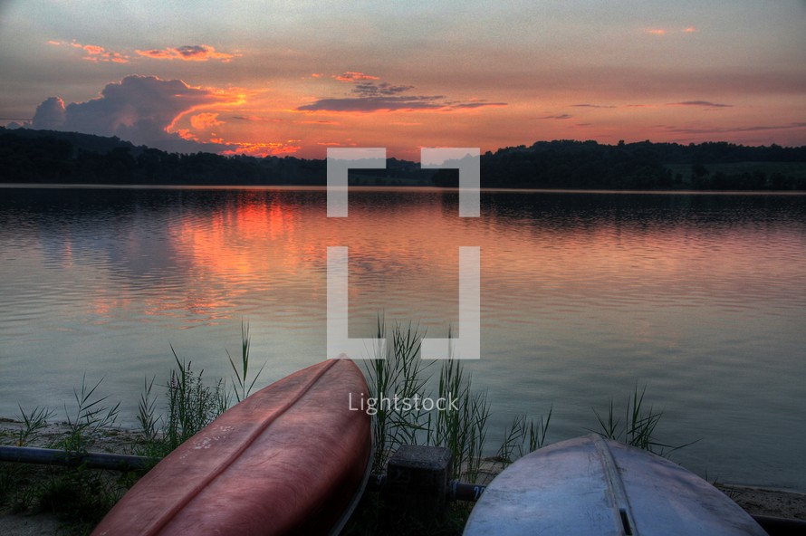 Kayaks on lake shore at sunset.