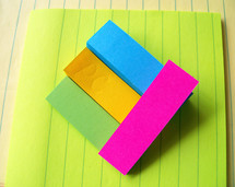 Various colors and types of paper with layers of colored sticky note paper raised above the surface to create a 3D effect with various colored sticky notes and paper.  