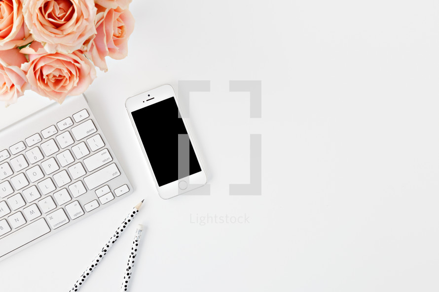 phone, computer keyboard, pencils, and peach roses on a desk 