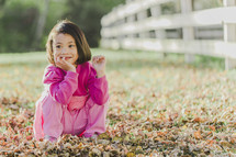 a young girl sitting in fall leaves 