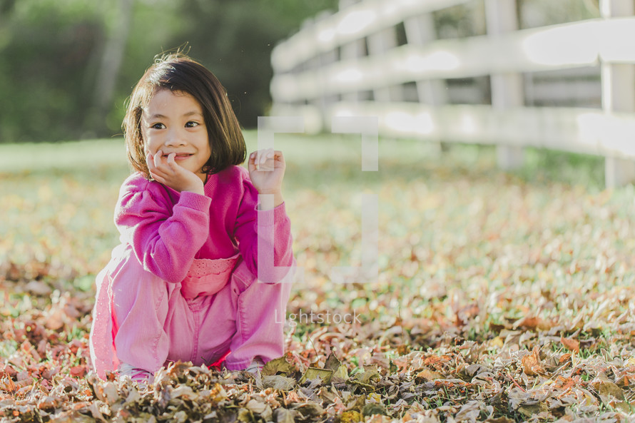 a young girl sitting in fall leaves 