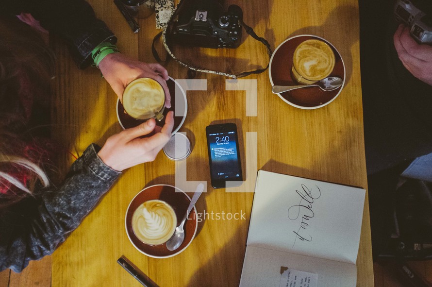 phone and camera on a table as they drink coffee 