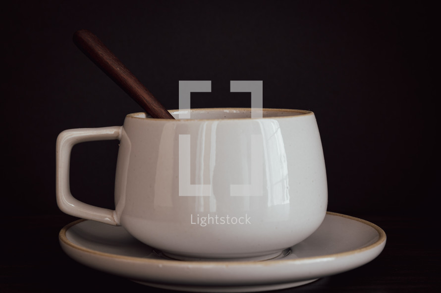 White mug and saucer with wooden spoon