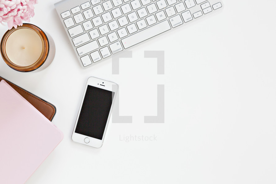 computer keyboard, candle, cellphone and pink notebook on a white desk 