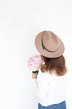 a woman in a hat holding a bouquet of pink flowers 