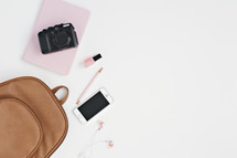 leather bag, cellphone, pink notebook, nail polish, pen, earbuds, and camera 