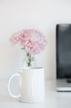 coffee cup, vase of flowers, and laptop computer on a desk 
