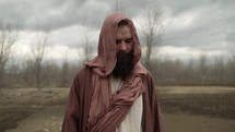 Jesus Christ or bible prophet like Noah, Moses, Elijah, Abraham or John the Baptist wearing brown robes and tunic, fasting, meditating, praying in nature in the wilderness.