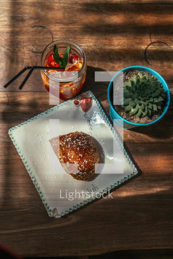 croissant and ice tea on a plate and succulent plant on a wood table 