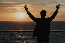 man with arms raised standing on a cruise ship 