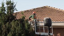 Gardener pruning a tree on a crane basket with protective wear jacket and full face shield