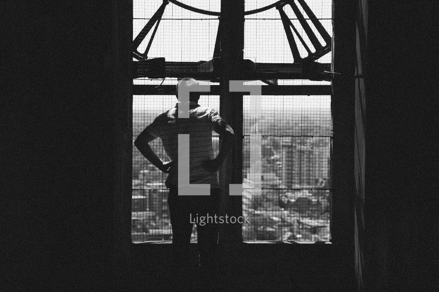 a man looking out a window at a clock tower at a city below 