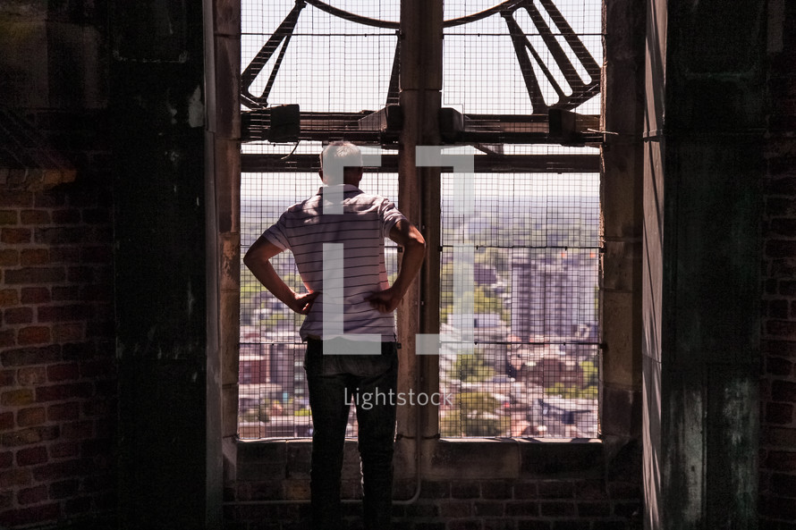 a man looking out a window in a clock tower at the city below 