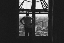 a man looking out a window at a clock tower at a city below 