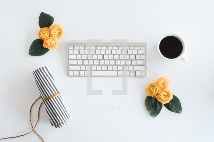 laptop keyboard, yellow roses, pen case, and coffee cup on a desk 