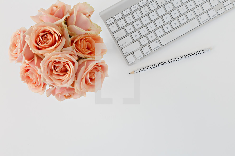 computer keyboard, pencils, and peach roses on a desk 