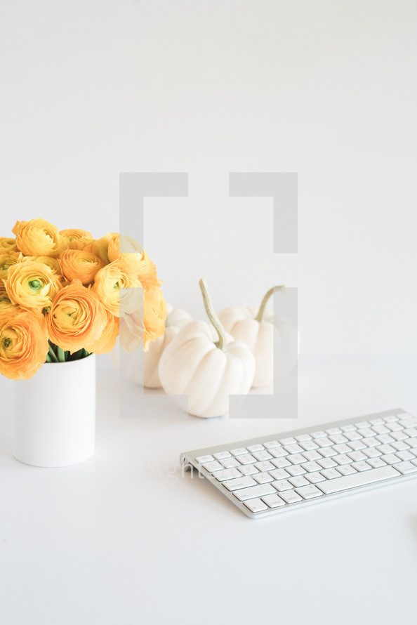 white pumpkins, yellow roses in a vase, computer keyboard on a desk 