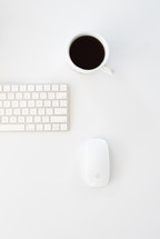 coffee mug, computer keyboard, and mouse on a white desk 