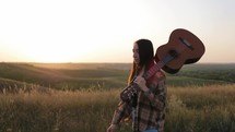 Beautiful young woman with guitar going at sunset. Woman musician holding guitar on sunset.