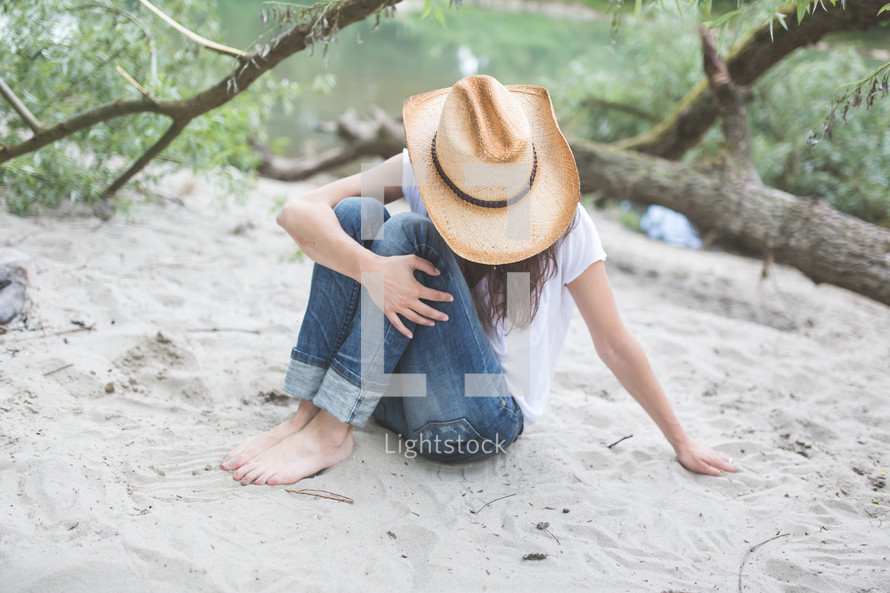woman in cowboy hat sitting on a beach 