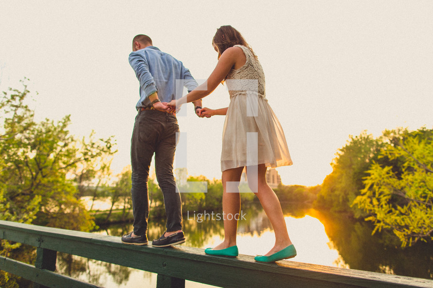 A couple holding hands and walking along the railing of a bridge
