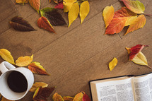 Open bible and a cup of coffee with a fall leaf border on wood