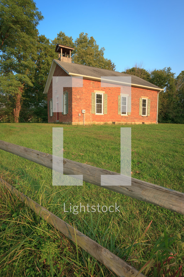 Old brick one room schoolhouse with grassy yard and wooden fence in Ohio 