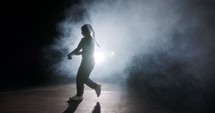 silhouette of a female dancer performing hip hop dance in slow motion with light and smoke background