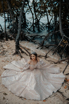 a woman in a crown and formal dress on a beach 