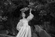 a woman in an elegant gown looking up at branches 