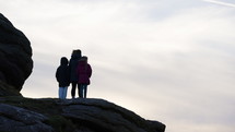 Young Family Together Outdoors Watching Sun Set On Dartmoor Rocks