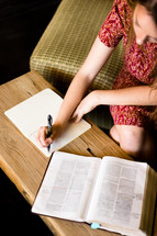 a woman writing notes in a journal while reading a Bible 