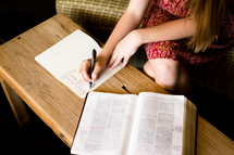 a woman writing notes in a journal while reading a Bible 