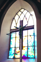 Crucifix in front of a stained glass window.