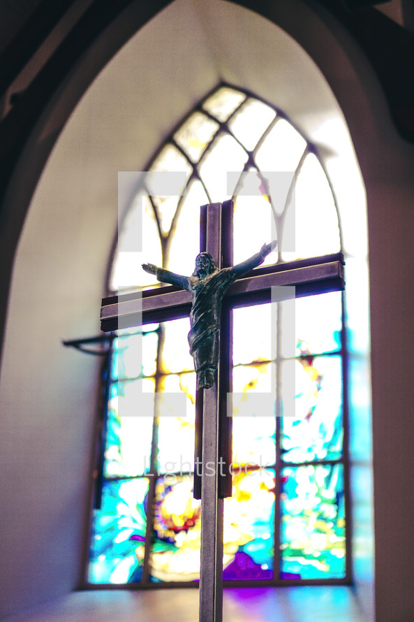 Crucifix in front of a stained glass window.