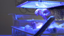 Father holding Jaundice newborns hand under UV blue light-hospital