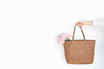 a woman carrying pink flowers in a bag 