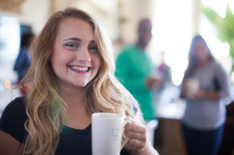A smiling young woman holding a cup of coffee.