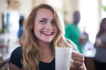 A smiling young woman holding a coffee cup.
