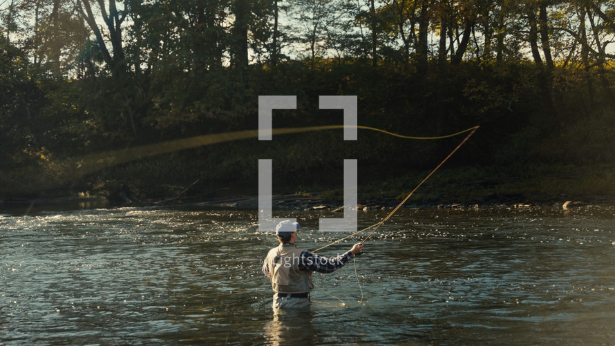 Young fly fisherman casting on a foggy river at sunrise